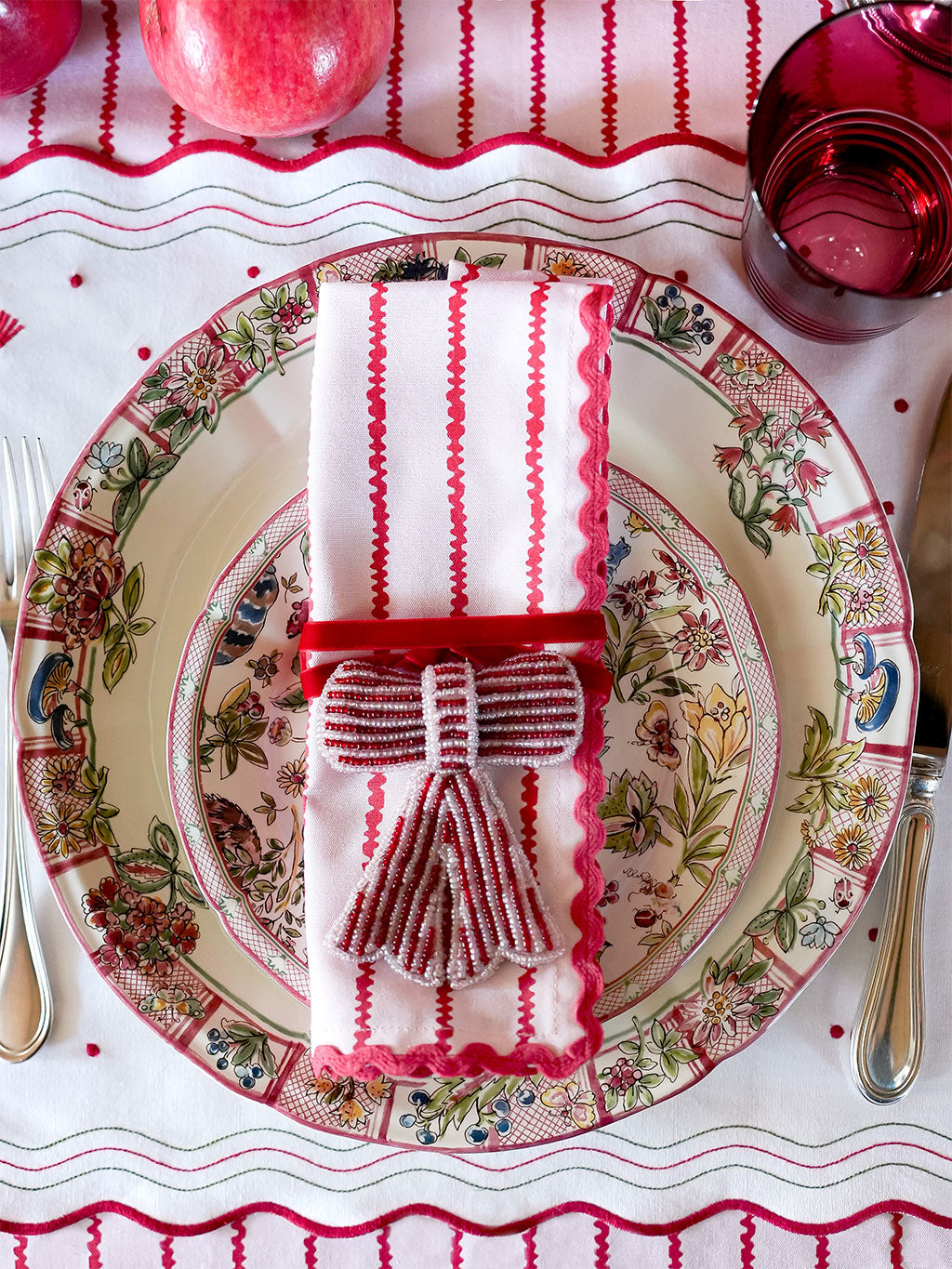 Decorative table setting with a patterned plate, red and white striped napkin, and red glassware.