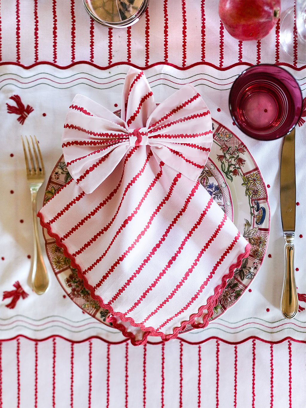 Decorative Christmas table setting with a striped red and white napkin, plates, and cutlery on a matching tablecloth.