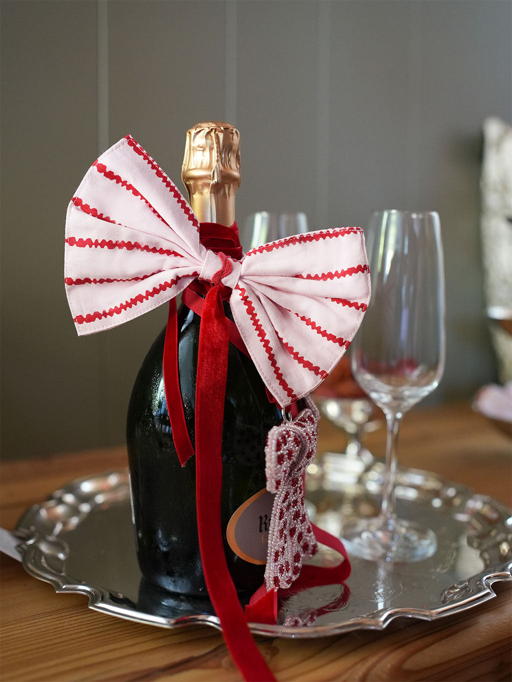 Bottle of champagne with a decorative bow on a silver tray with wine glasses in the background.