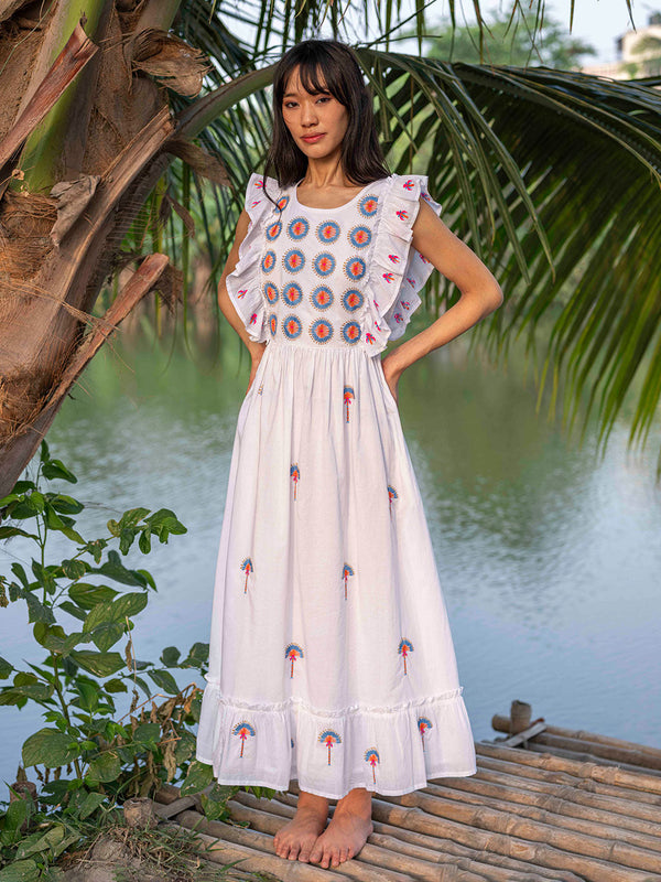 Model wearing the fitted Pernilla embroidered midi boho dress in organic cotton, showcasing the breezy summer silhouette in a tropical luxury resort