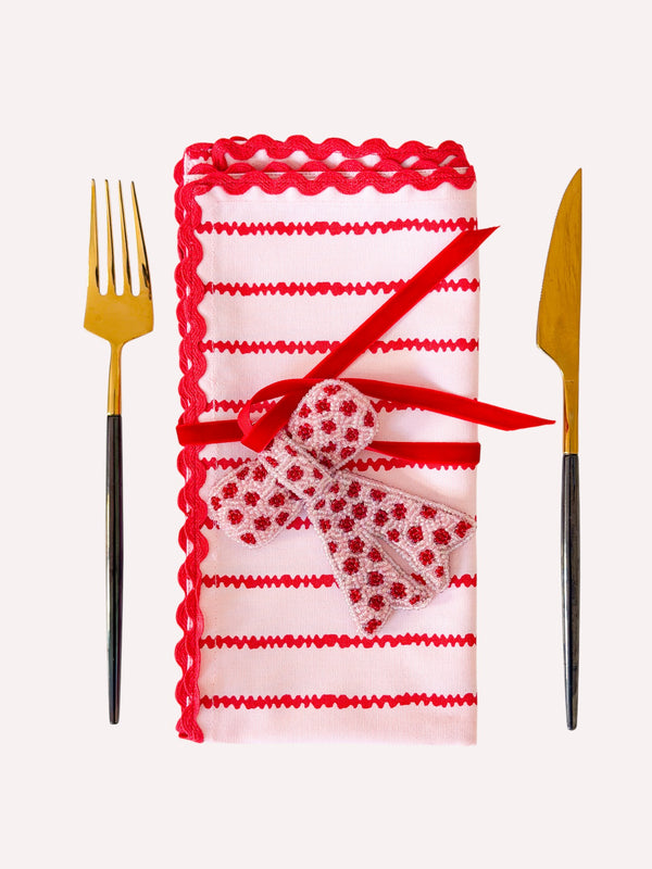 Candy cane colored Christmas napkin decorated with a bow ornament and a velvet ribbon