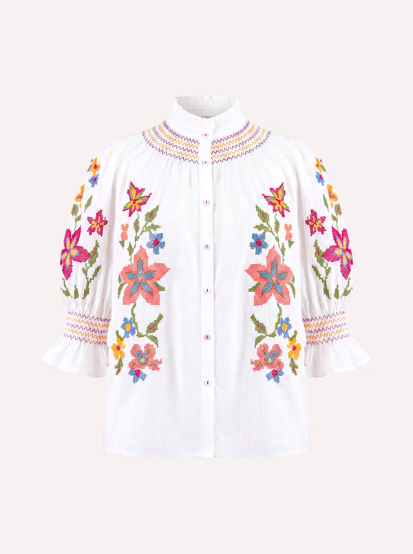White button-up blouse with colorful floral embroidery on the front and sleeves, featuring a high pleated collar and ruffled three-quarter sleeves, shown on a light beige background.