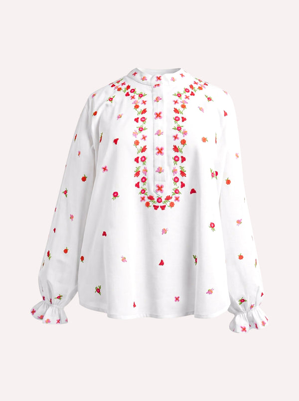 A white long-sleeve blouse with colorful floral embroidery around the neckline and scattered across the fabric, featuring ruffled cuffs, shown against a light beige background.