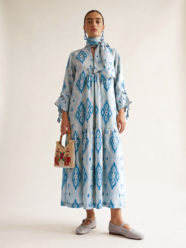 Woman styling the light blue Catmint dress with a matching ikat scarf belt tied around the neck and a bamboo handle bag.