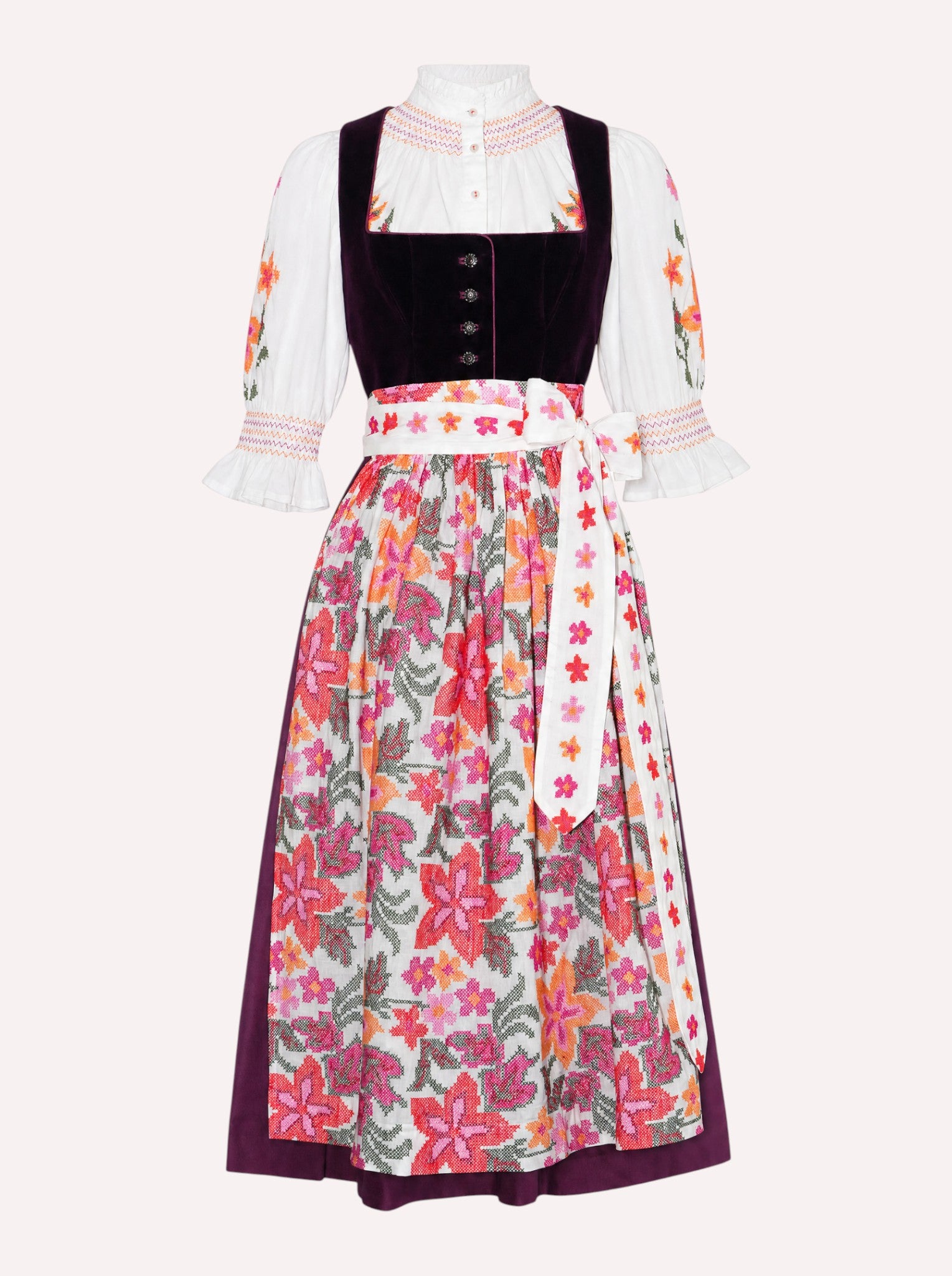 Nimo x Münchner Manufaktur dirndl apron with dense red and orange floral cross-stitch embroidery styled over a burgundy dirndl.