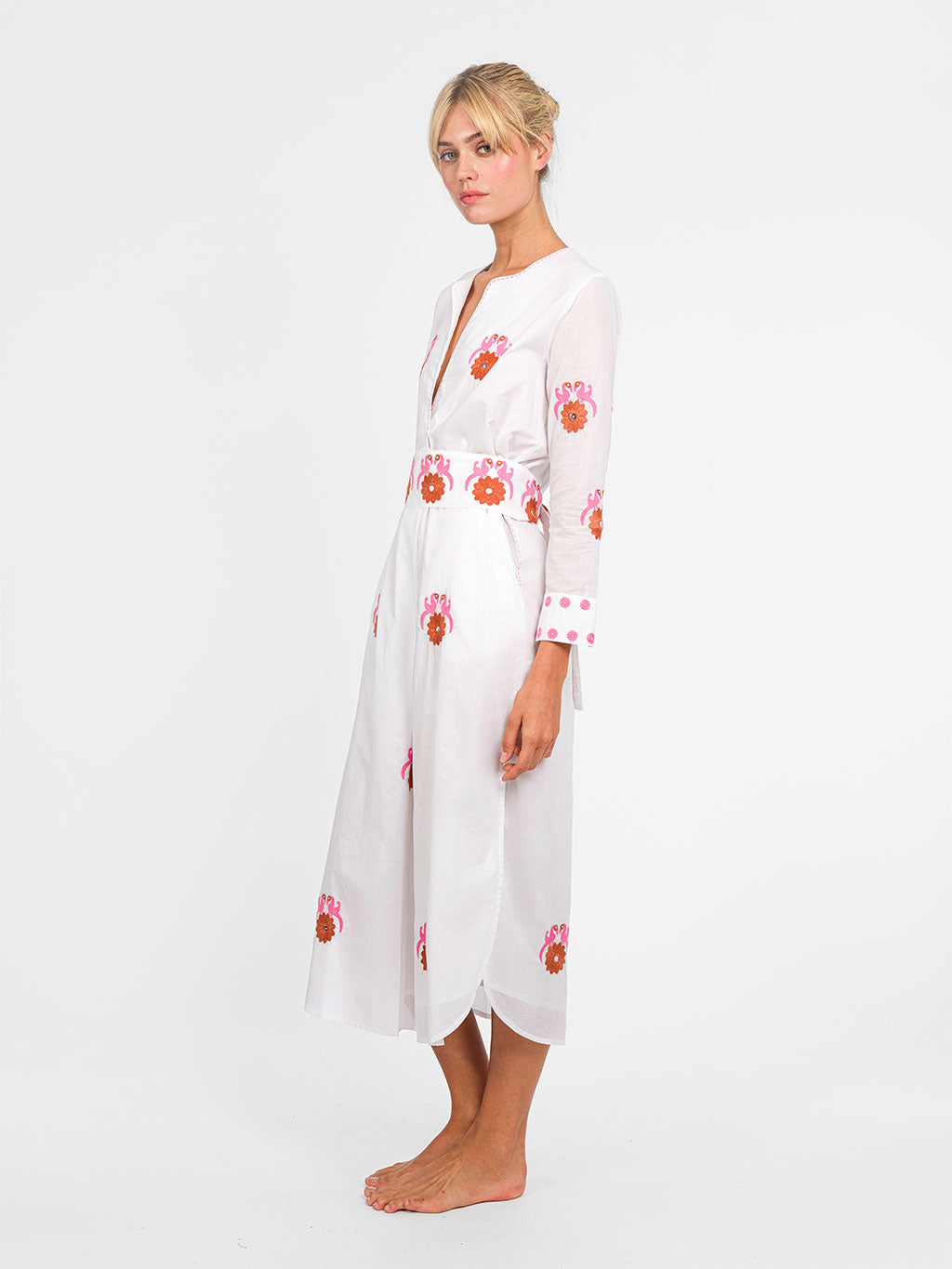 Side view of the side slit and the rhythmic bird embroidery along the hem of the white midi dress.