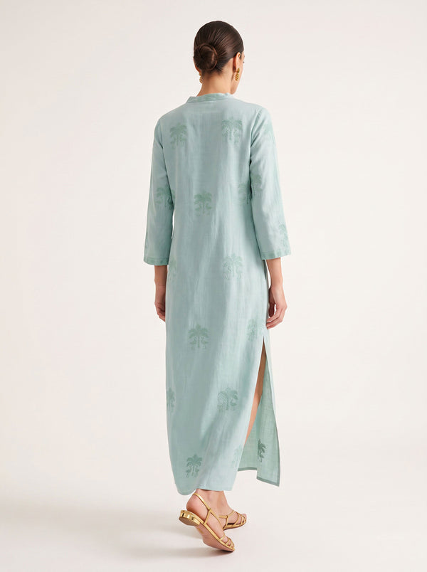 A woman viewed from the back wearing a light mint green kurta maxi dress with subtle tonal floral embroidery and a side slit, paired with gold sandals, against a plain off-white studio background.
